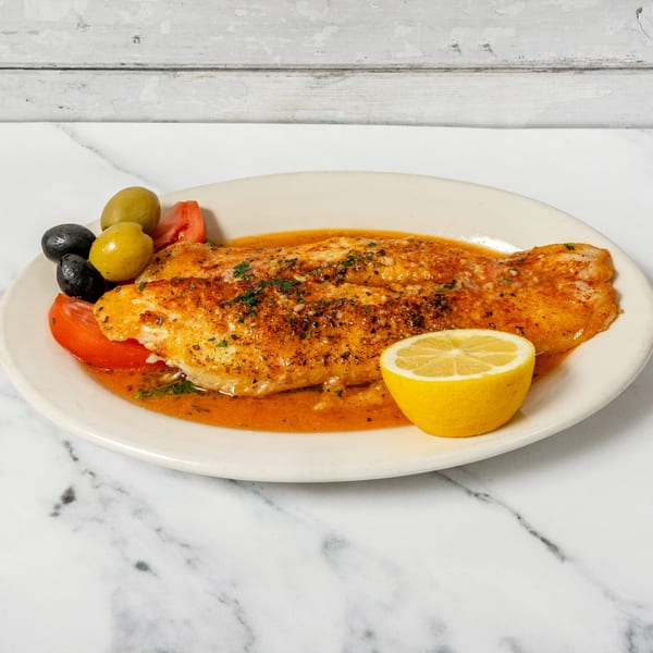 Seasoned fish fillet in orange sauce with olives, tomato slices, and a lemon wedge.