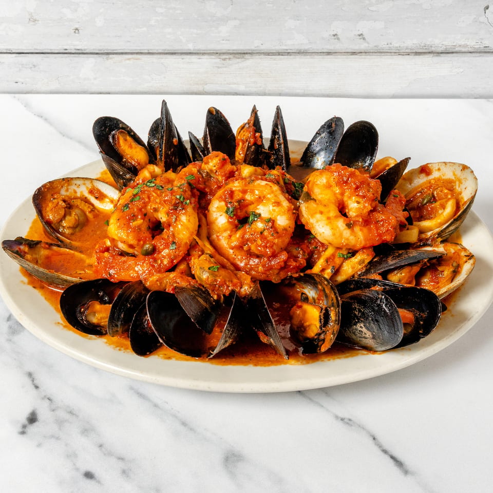 Platter of mussels, clams, and shrimp in a rich tomato sauce, garnished with fresh herbs.