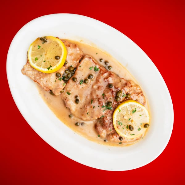 Creamy chicken piccata with capers, lemon, and parsley on a white oval plate.