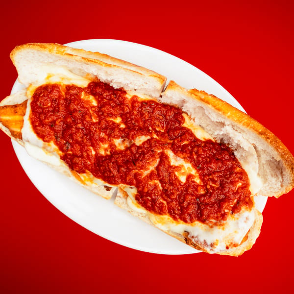 Open sub sandwich with rich red sauce and melted cheese on a white plate.