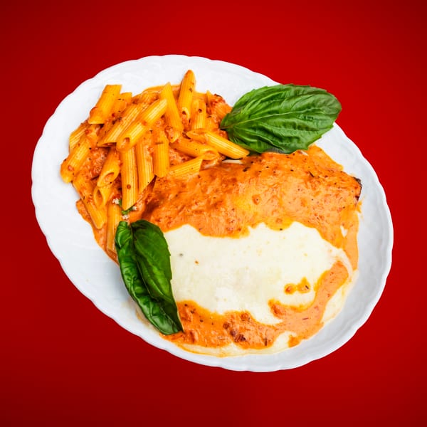 Penne pasta and a cheesy baked entree with red sauce and fresh basil on a white plate.