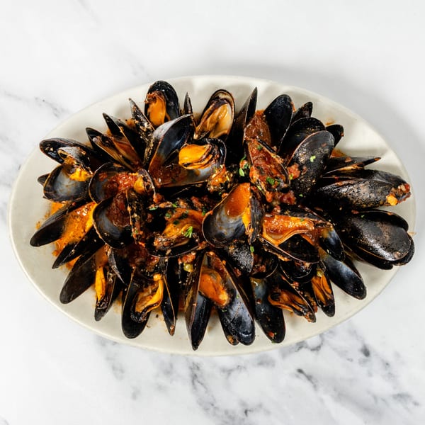 Steamed mussels in a rich red tomato sauce, garnished with fresh herbs, served on a white platter.