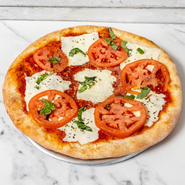 Classic Margherita pizza with sliced tomatoes, fresh mozzarella, and basil on a metal tray.