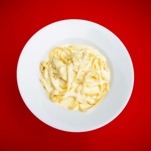 Creamy fettuccine pasta on a white plate against a vibrant red background.