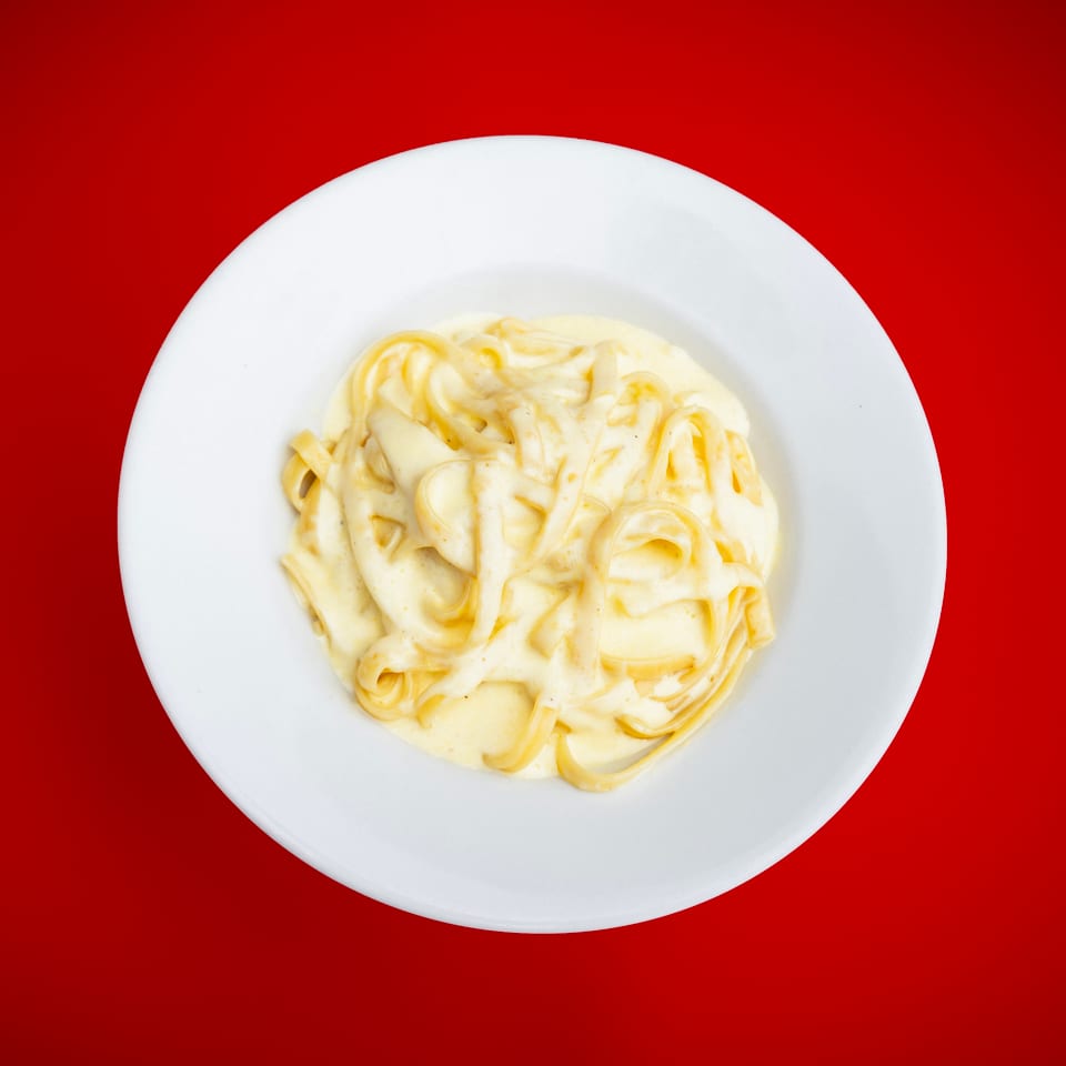 Creamy fettuccine pasta on a white plate against a vibrant red background.