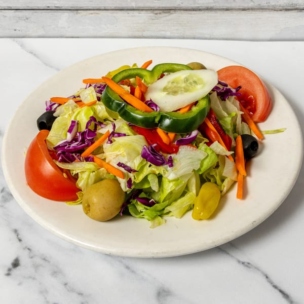 Colorful garden salad with mixed greens, tomatoes, bell peppers, carrots, cucumbers, and olives on a white plate.