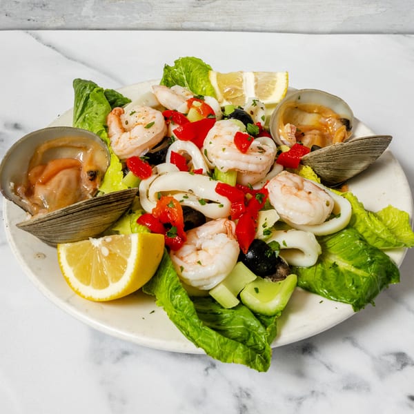 Plate of vibrant seafood salad with shrimp, calamari, clams, colorful vegetables, and lemon.
