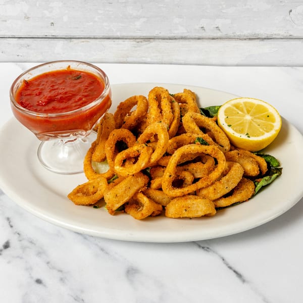 Fried calamari rings with marinara sauce and a lemon wedge on a white plate.