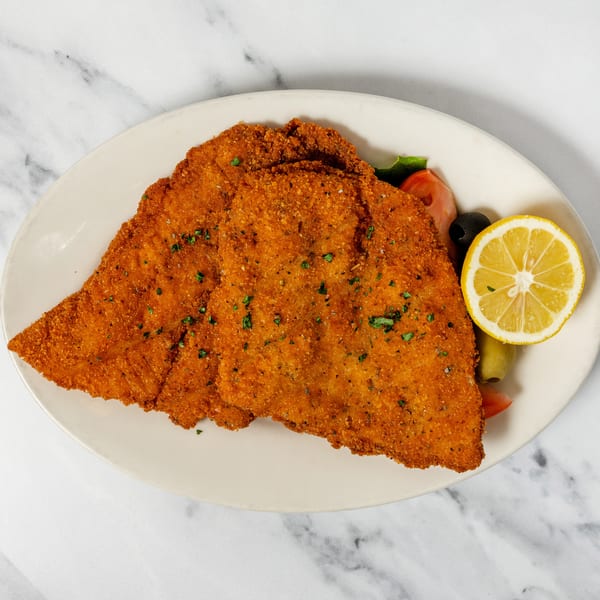 Crispy breaded cutlets garnished with a lemon slice, olives, and fresh tomatoes.