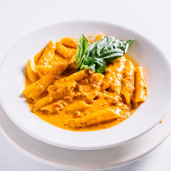 Penne pasta in creamy orange sauce, garnished with fresh basil, served in a white bowl.