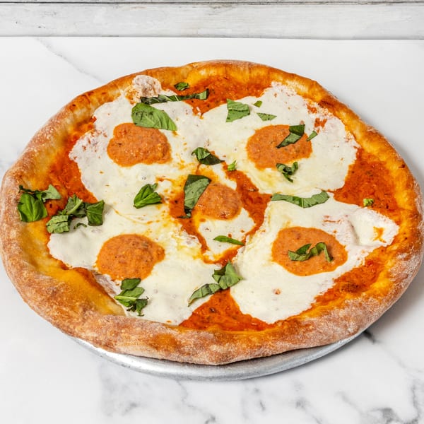 Round pizza with melted mozzarella, red sauce, fresh basil, and orange sauce dollops on a marble surface.