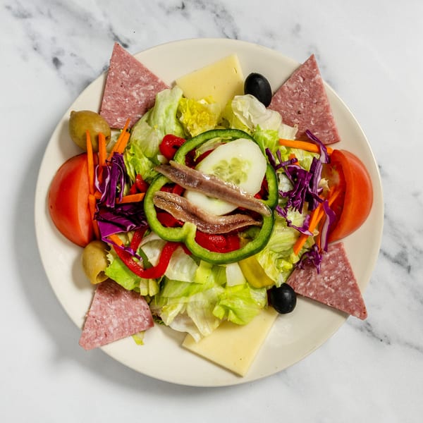 A vibrant salad featuring lettuce, salami, cheese, tomatoes, olives, anchovies, and mixed vegetables.