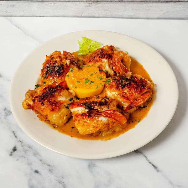 Golden-brown shrimp and polenta in a creamy orange sauce, garnished with parsley on a white plate.