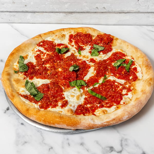 A whole pizza with dollops of white cheese, red sauce, and fresh basil on a metal pan.