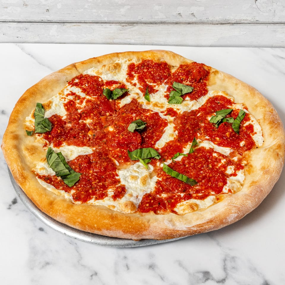 A whole pizza with dollops of white cheese, red sauce, and fresh basil on a metal pan.