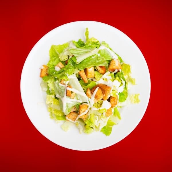 Caesar salad with fresh green lettuce, golden croutons, and creamy white dressing on a white plate.