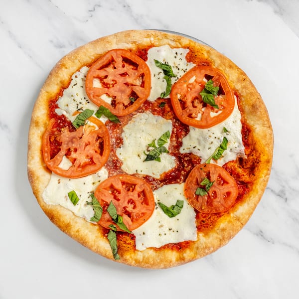 Classic Margherita pizza with sliced tomatoes, fresh mozzarella, and basil on marble.