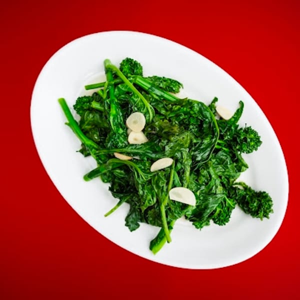 Green sautéed broccoli rabe with sliced garlic on a white oval plate.