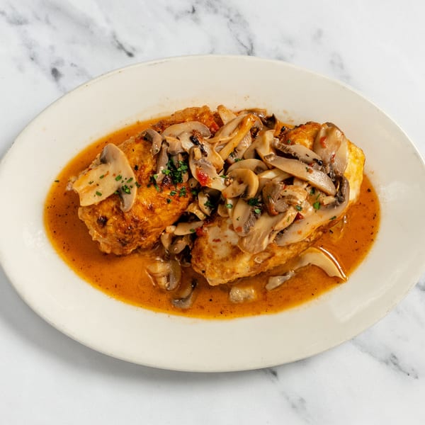 Two golden chicken breasts topped with sliced mushrooms and a savory orange sauce on a white plate.