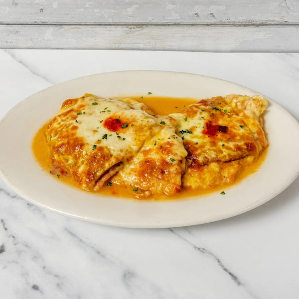 Two cheesy baked pasta rolls in a rich orange sauce, garnished with fresh herbs on a white plate.