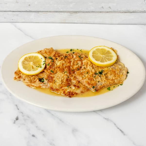 Golden-brown chicken cutlets in lemon butter sauce, garnished with parsley and lemon slices.